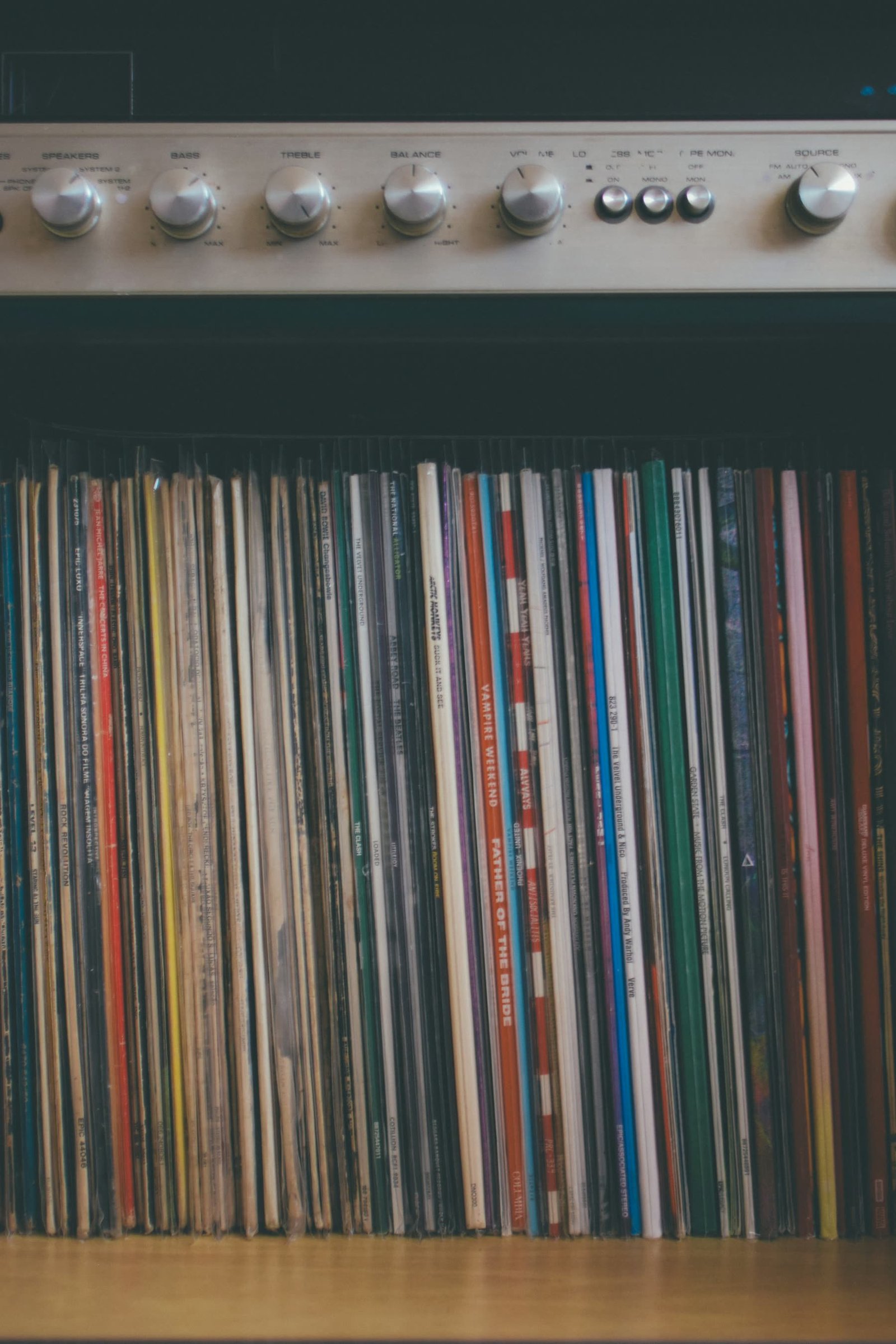 A shelf of vinyl records beneath a vintage stereo receiver