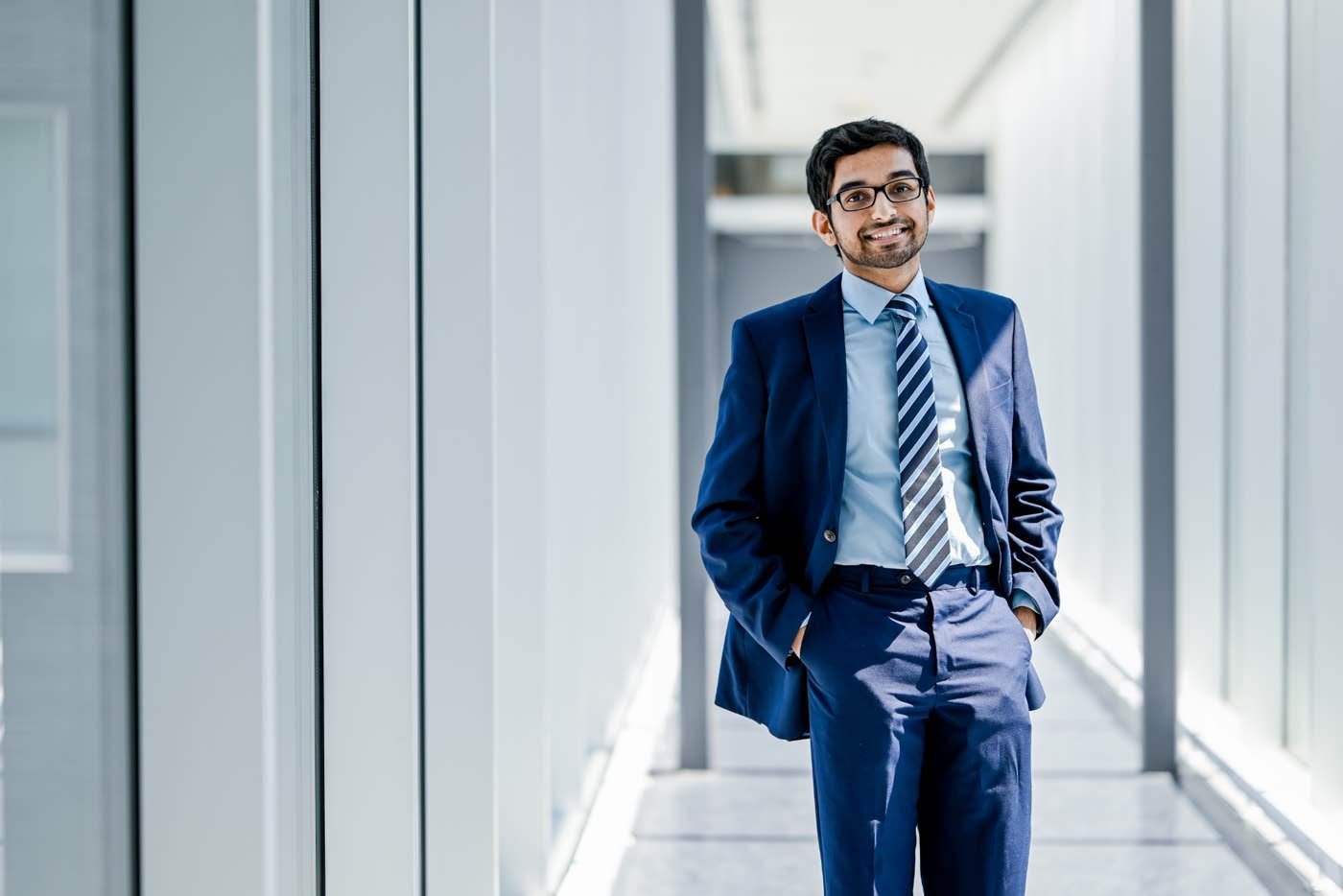 Nabeen walking through a bright office corridor in a navy suit